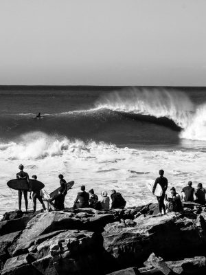 Black and white image of surfers observing waves at Taghazout beach.