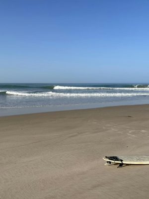 Surfboard on a sandy beach in Dakhla with ocean waves and clear blue sky.