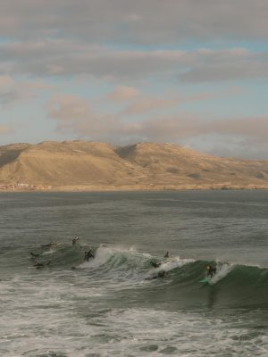 Surfers riding waves at Imsouane beach, Morocco under a bright sky.