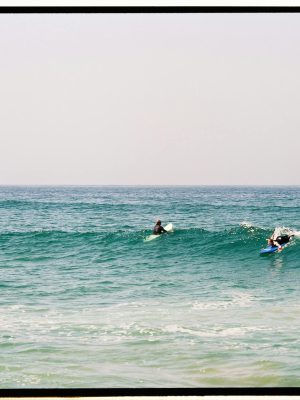 Two surfers catching waves in the vibrant blue ocean of Morocco.